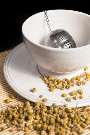 Tea strainer with dry chamomile in white cup in preparation of the chamomile tea の写真素材