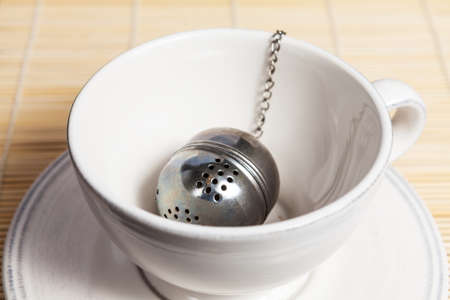 Metal round tea strainer on the chain, in the white tea cupの写真素材