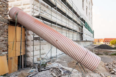 Reconstruction site, wall in scaffolding with green protective cloth, with pipe used to lower...