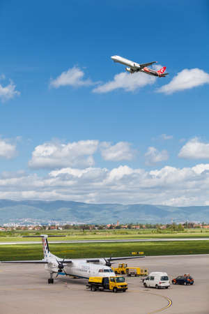 Turkish Airlines Euroleague Airbus A321-231 flying over Croatia Airlines Dash-8 parked on tarmac on Pleso airport in Zagreb, Croatiaのeditorial素材