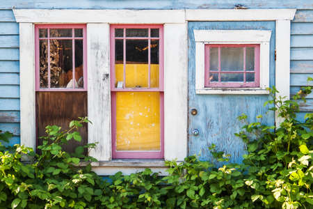 Front side of an abandoned country house with damaged doors and windows on a blue wooden facadeのeditorial素材