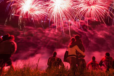 Big fireworks with young romantic couple in love in front, holding each other and watching the showの写真素材