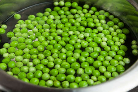 Green peas thawed and cooking in the water in the metal pot on the stoveの写真素材