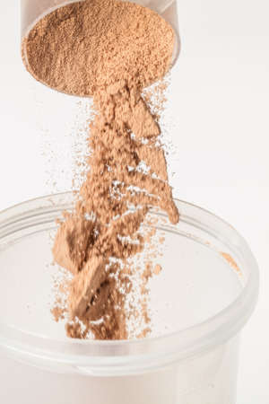 Scoop of chocolate whey isolate protein tossed into plastic white shaker, with focus on the protein in the scoop and falling protein blurredの写真素材