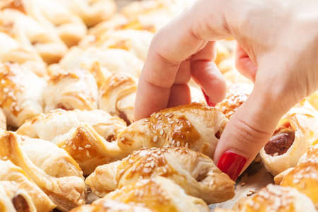 Closeup of a female hand reaching for freshly baked frankfurter sausages battered in puffed French pastryの写真素材