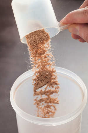 Scoop of chocolate whey isolate protein tossed into plastic white shakerの写真素材