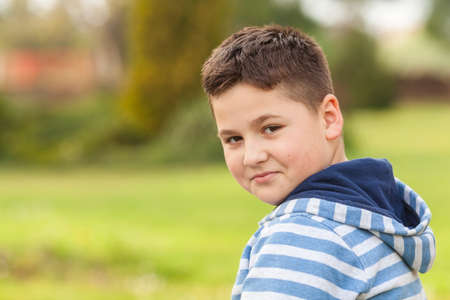 Portrait of a seven years old young caucasian boy in the shirt with the blue and white stripes in the parkの写真素材