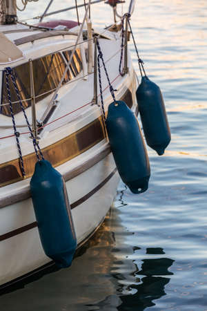 Side of a yacht with three blue fenders, used to protect the boat from hiting the pier or another...