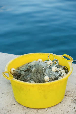 Gray fishing net on the heap in the yellow plastic container, with blue sea in the background