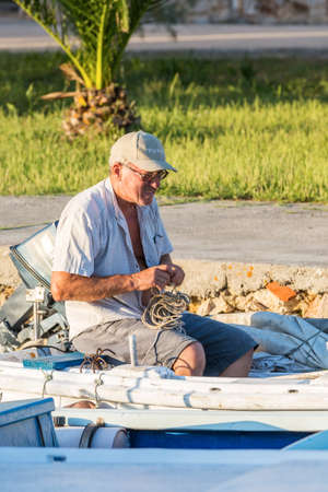VELI IZ, CROATIA - AUGUST 15, 2014: Fishermen's working on his boat parked and tied in city harbour in Veli Iz, on island Iz, with yacht in the marina in the background. Veli Iz is largest settlement on the island Iz.のeditorial素材