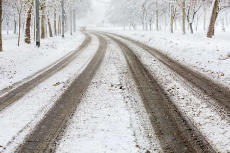 Traces of car tires on the street during heavy snowstorm, tracks visible and the road still not cleaned, presenting danger for drivers -  accident waiting to happenの写真素材