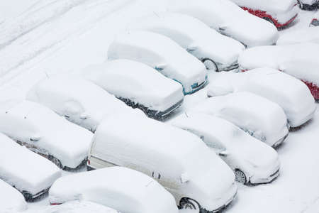 Cars covered in snow on a parking lot in the residential area during December snowfallの写真素材