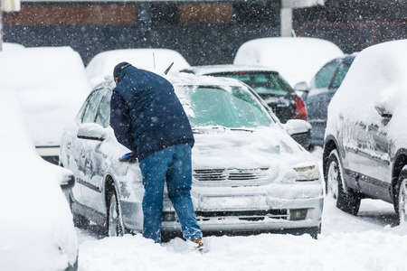 Man scraping frozen snow from the car windows during the heavy snowfallの写真素材