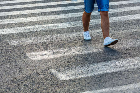 Abstract image of a man on zebra crossing diagonally over an asphalt road, only legs visible, left...