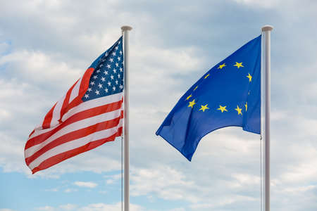 Flags of Un ited States of America and European Union hanging on poles, waving in the windの写真素材