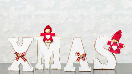White wooden letters on brown wooden table forming word XMAS with ribbons and red figures around themの写真素材