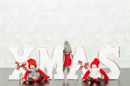 White wooden letters on brown wooden table forming word XMAS with ribbons and red figures around themの写真素材