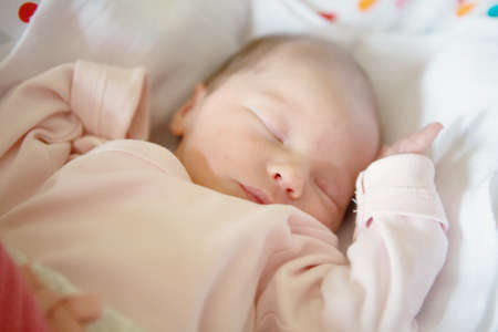 Newborn baby girl sleeping in her crib, lit by the morning sunの写真素材