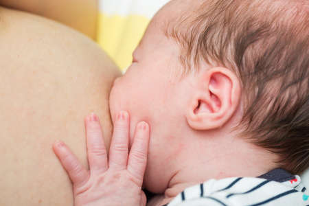 Eight days old newborn baby girl during breastfeeding, helping herself with her hand