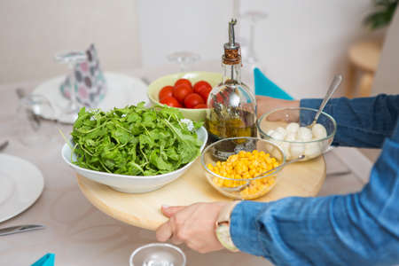 Woman bringing a wooden tray with fresh organic arugula, tomato and corn salad and mozzarella balls...