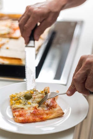 Man's hands cutting slices of homemade pizza with a knife and putting it on a plate; pizza with...