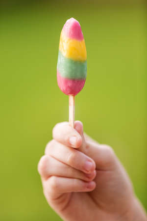 Girl's hand holding refreshing fruit ice cream on a stick; in red, green and yellow colors