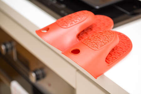 Red silicon oven gloves, protection from heat, above the stoveの写真素材