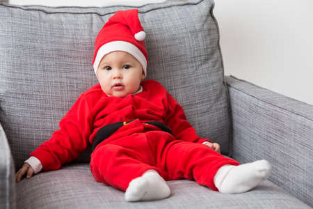 Seven months old baby girl in Santa Claus dress sitting on a sofaの写真素材