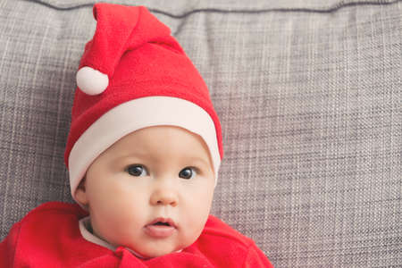 Seven months old baby girl in Santa Claus dress sitting on a grey sofaの写真素材