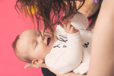 Mother holding baby daughter in the arms and playing with her, girl smiling and touching her hair