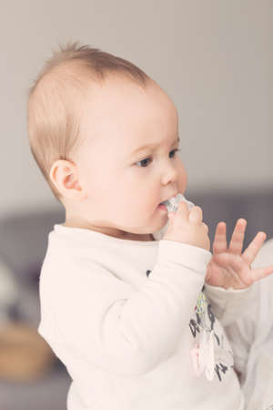 Eight months old baby girl bringing her pacifier to her mouth and sucking it の写真素材