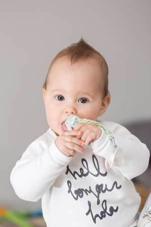 Eight months old baby girl bringing her pacifier to her mouth and sucking itの写真素材