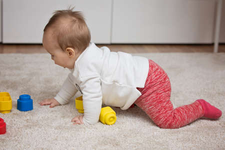 Nine months old baby girl playing with her toys on the floor and crawlingの写真素材