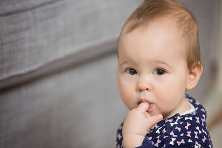 Nine months old baby girl sticking her finger in the mouth to ease the pain of teething, with eyes...