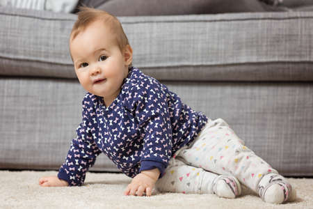 Nine months old baby girl on the floor preparing to crawl in front of the sofaの写真素材