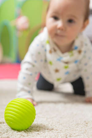 Nine months old baby girl crawling on the floor towards the green toy ball; shallow depth of field, focus on the ballの写真素材