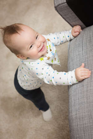 Nine months old baby girl standing on her feet in an effort to climb up the sofa; baby just learnt...