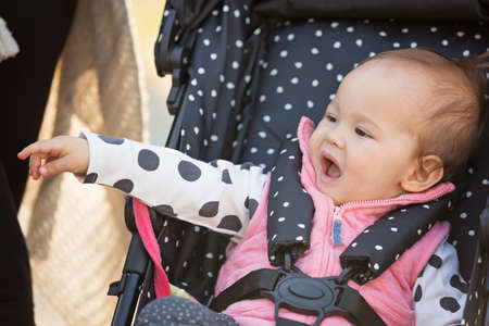 One year old baby girl sitting in the dotted stroller, pointing her finger at something and laughing with mouth wide openの写真素材