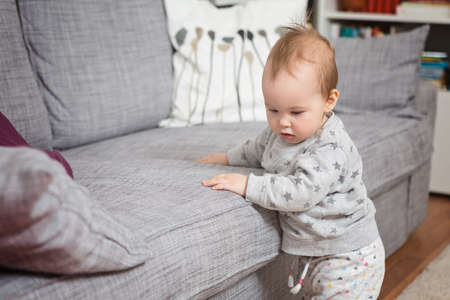 Eleven months old baby girl standing by the sofaの写真素材