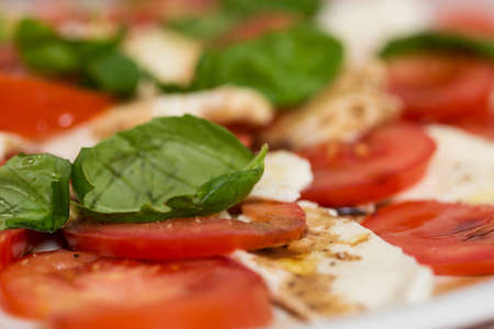 Tomato and mozzarella salad with basil leaves, sprinkled with pepper, olive oil and acceto balsamico on the white plateの写真素材