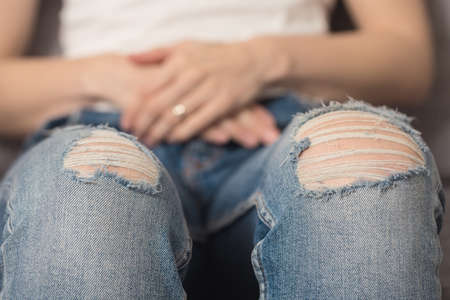 Girl with denim fabric pants, sitting on the sofa; denim torn on the knees and threads coming apart