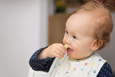 One year old baby girl feeding herself with her fingers, baby led weaning; concept of motherhood and...