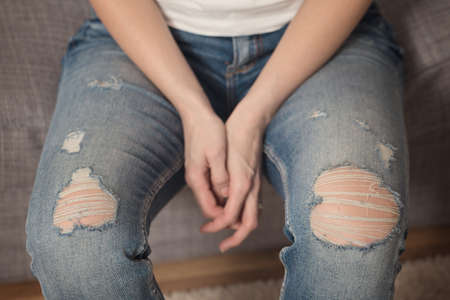 Girl with denim fabric pants, sitting on the sofa; denim torn on the knees and threads coming apartの写真素材