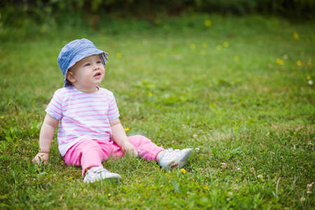 Fourteen months old baby girl sitting on the grass on the sunny summer day