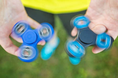 Girl holding blue and black fidget spinners in her hands, view from above; both gadgets spinningの写真素材