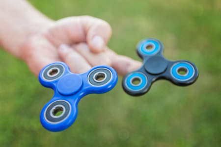 Man holding two fidget spinners on his fingers against the blurred grass backgroundの写真素材
