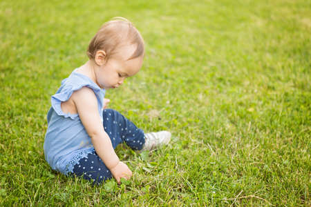 Fourteen months old baby girl sitting in the shadow on the grass on the sunny summer dayの写真素材