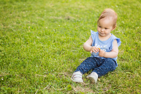 Fourteen months old baby girl sitting in the shadow on the grass on the sunny summer dayの写真素材
