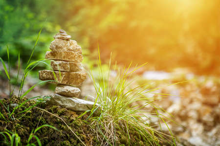 Balanced pyramide made of small rock stones on the shore of blue water of mountain river, with sun light leakの写真素材