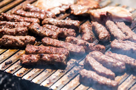 Grilling minced meat on a barbecue grill with coal; outdoors picnic with minced pork meat rolls (also known as mici,   mititei, cevapi or cevapcici)の写真素材